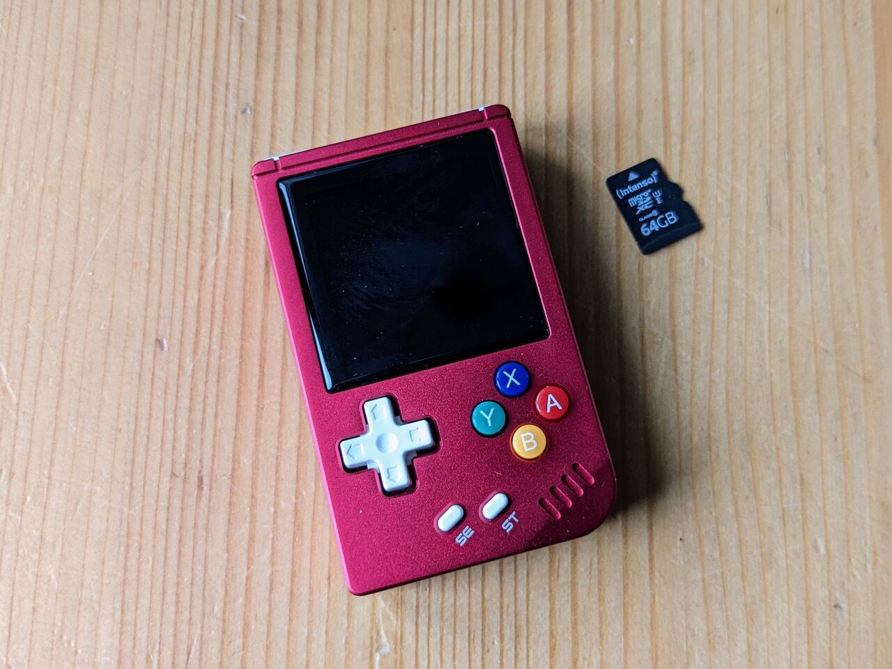 Anbernic RG Nano handheld console (In pinkish red) next to a Micro SD card to show how tiny it is - It's about 4cm wide and 7cm long)
